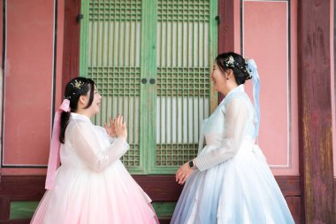 Haziran 'da Seul' de, yirmili yaşlarda iki Koreli kadın açık bir yaz gökyüzünün altında, sevimli pembe ve gökyüzü mavisi Hanbok giymiş, geleneksel Gyeongbokgung Sarayı 'nın ahşap penceresinin önünde gülüyor..