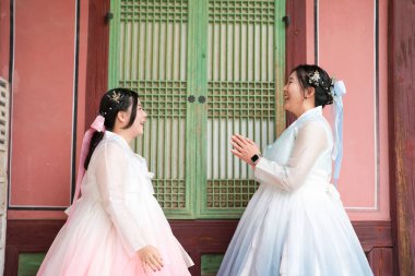 Haziran 'da Seul' de, yirmili yaşlarda iki Koreli kadın açık bir yaz gökyüzünün altında, sevimli pembe ve gökyüzü mavisi Hanbok giymiş, geleneksel Gyeongbokgung Sarayı 'nın ahşap penceresinin önünde gülüyor..