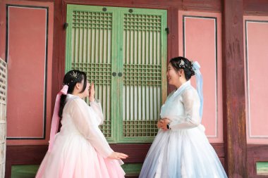 Haziran 'da Seul' de, yirmili yaşlarda iki Koreli kadın açık bir yaz gökyüzünün altında, sevimli pembe ve gökyüzü mavisi Hanbok giymiş, geleneksel Gyeongbokgung Sarayı 'nın ahşap penceresinin önünde gülüyor..