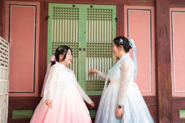 Haziran 'da Seul' de, yirmili yaşlarda iki Koreli kadın açık bir yaz gökyüzünün altında, sevimli pembe ve gökyüzü mavisi Hanbok giymiş, geleneksel Gyeongbokgung Sarayı 'nın ahşap penceresinin önünde gülüyor..