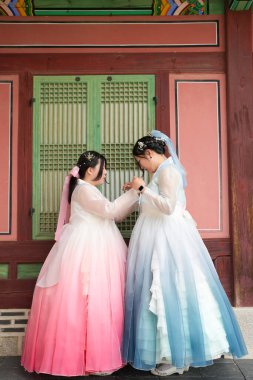 Haziran 'da Seul' de, yirmili yaşlarda iki Koreli kadın açık bir yaz gökyüzünün altında, sevimli pembe ve gökyüzü mavisi Hanbok giymiş, geleneksel Gyeongbokgung Sarayı 'nın ahşap penceresinin önünde gülüyor..