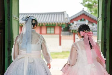 Haziran 'da Seul' de, yirmili yaşlarda iki Koreli kadın açık bir gökyüzü altında Gyeongbokgung Sarayı 'ndaki geleneksel ahşap bir binanın önünde yürürken sevimli pembe ve gökyüzü mavisi bir Hanbok giyiyorlardı..