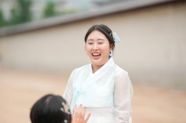 Haziran 2025 'te Seul' de, 20 'li yaşlarda iki Koreli kadın pembe ve gökyüzü mavisi Hanbok giyerek Gyeongbokgung Sarayı' nın süslü kapılarının önünde gülüp sohbet ediyorlar..