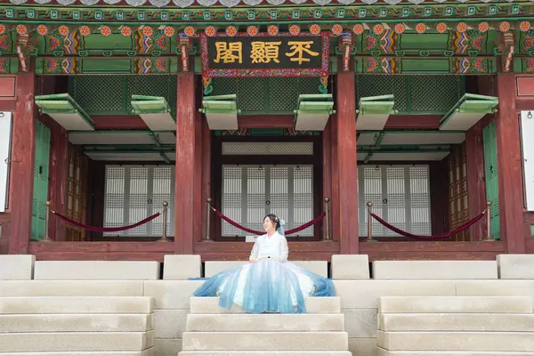 Haziran 'da Seul' de, yirmili yaşlarda Koreli bir kadın Gyeongbokgung Sarayı 'ndaki geleneksel bir binanın önünde oturuyor. Gökyüzü mavisi bir hanbok giyiyor ve tarihi mimariye hayran..