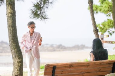 Haziran 2025 'te, 50' li yaşlarının sonlarında bir Koreli erkek ve kadın deniz kenarındaki bir bankta oturup esinti, okyanus manzarası ve Incheon Metropolitan City 'nin sakin ortamının tadını çıkarırken sohbet ediyor ve gülümsüyor..
