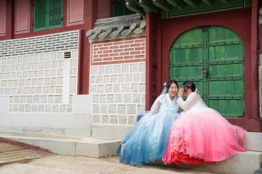 Haziran 'da Seul' de, yirmili yaşlarda iki Koreli kadın açık bir yaz gökyüzü altında mutlu bir şekilde sohbet ederken Gyeongbokgung Sarayı 'nın geleneksel ahşap kapısında oturuyorlar..