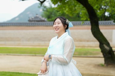 Haziran 2025 'te Seul' de, 20 'li yaşlarda iki Koreli kadın pembe ve gökyüzü mavisi Hanbok giyerek Gyeongbokgung Sarayı' nın süslü kapılarının önünde gülüp sohbet ediyorlar..