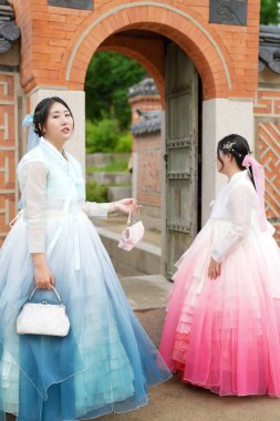 Haziran 2025 'te Seul' de, 20 'li yaşlarda iki Koreli kadın pembe ve gökyüzü mavisi Hanbok giyerek Gyeongbokgung Sarayı' nın geleneksel tuğla kapısının önünde duruyorlardı..