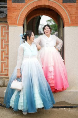 Haziran 2025 'te Seul' de, 20 'li yaşlarda iki Koreli kadın pembe ve gökyüzü mavisi Hanbok giyerek Gyeongbokgung Sarayı' nın geleneksel tuğla kapısının önünde duruyorlardı..