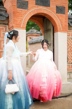 Haziran 2025 'te Seul' de, 20 'li yaşlarda iki Koreli kadın pembe ve gökyüzü mavisi Hanbok giyerek Gyeongbokgung Sarayı' nın geleneksel tuğla kapısının önünde duruyorlardı..