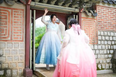 Haziran 2025 'te Seul' de, 20 'li yaşlarda iki Koreli kadın pembe ve gökyüzü mavisi Hanbok giyerek Gyeongbokgung Sarayı' nın geleneksel tuğla kapısının önünde duruyorlardı..