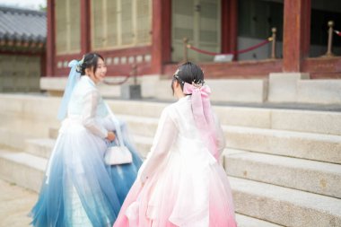 Haziran 2025 'te Seul' de, 20 'li yaşlarda iki Koreli kadın pembe ve gökyüzü mavisi Hanbok giyerek Gyeongbokgung Sarayı' nın geleneksel tuğla kapısının önünde duruyorlardı..