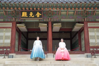 20 'li yaşlarda iki Koreli kadın pembe ve gökyüzü mavisi Hanbok giyerek Haziran 2025' te Seul 'de Gyeongbokgung Sarayı' nın önünde dururlar..