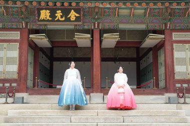 20 'li yaşlarda iki Koreli kadın pembe ve gökyüzü mavisi Hanbok giyerek Haziran 2025' te Seul 'de Gyeongbokgung Sarayı' nın önünde dururlar..