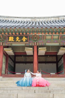 20 'li yaşlarda, pembe ve gökyüzü mavisi Hanbok giyen iki Koreli kadın, Haziran 2025' te Seul 'de Gyeongbokgung Sarayı' nın ön cephesinde oturuyorlar..