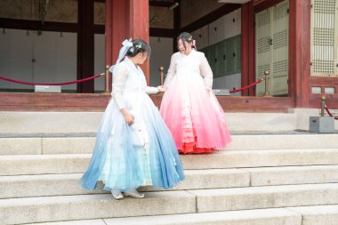 Haziran 2025 'te Seul' de, 20 'li yaşlarda iki Koreli kadın pembe ve gökyüzü mavisi Hanbok giyerek Gyeongbokgung Sarayı' nın geleneksel tuğla kapısının önünde duruyorlardı..