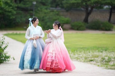 Haziran 2025 'te Seul' de, 20 'li yaşlarda iki Koreli kadın pembe ve gökyüzü mavisi Hanbok giyerek Gyeongbokgung Sarayı' nın süslü kapılarının önünde gülüp sohbet ediyorlar..