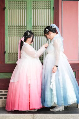 Haziran 2025 'te Seul' de, 20 'li yaşlarda iki Koreli kadın pembe ve gökyüzü mavisi Hanbok giyerek Gyeongbokgung Sarayı' nın geleneksel tuğla kapısının önünde duruyorlardı..