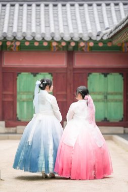 Haziran 'da Seul' de, 20 'li yaşlarında iki Koreli kadın Gyeongbokgung Sarayı' ndaki tarihi bir salonun önünde sevimli pembe ve gökyüzü mavisi Hanbok giyip açık bir yaz gökyüzü altında kameraya doğru zarif sırtlarını döndüler..