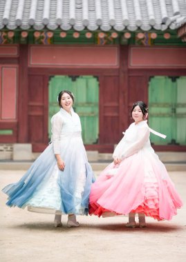 Yirmili yaşlarda iki Koreli kadın, Gyeongbokgung Sarayı 'nda, yumuşak, berrak bir yaz gökyüzünün altında, sevimli pembe ve gökyüzü mavisi Hanbok' a zarif bir şekilde dönüp bakıyorlar. Seul, Haziran.