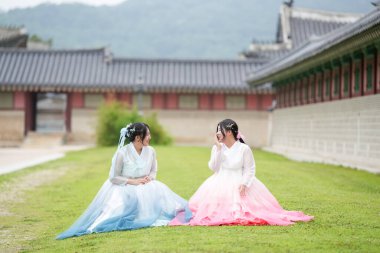 Yirmili yaşlarda iki Koreli kadın Gyeongbokgung Sarayı 'nın bahçesinde, sevimli pembe ve gökyüzü mavisi Hanbok giyip açık bir yaz gökyüzü altında huzurlu anların tadını çıkarıyorlar. Seul, Haziran.
