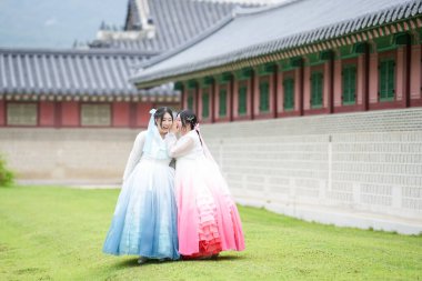 Yirmili yaşlarda iki Koreli kadın Gyeongbokgung Sarayı 'ndaki tarihi bir salonun önünde, açık bir yaz gökyüzü altında, pembe ve gökyüzü mavisi bir Hanbok giyip, çimlerin üzerinde yürüyorlar. Seul, Haziran.