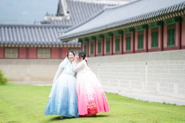Yirmili yaşlarda iki Koreli kadın Gyeongbokgung Sarayı 'ndaki tarihi bir salonun önünde, açık bir yaz gökyüzü altında, pembe ve gökyüzü mavisi bir Hanbok giyip, çimlerin üzerinde yürüyorlar. Seul, Haziran.