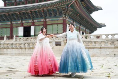 Yirmili yaşlardaki iki Koreli kadın, açık bir yaz gökyüzü altında güzel pembe ve gökyüzü mavisi Hanbok giyen tarihi mimarinin ortasında, Gyeongbokgung Sarayı 'nda güneşli bir plazada zarif bir şekilde dans ediyorlar. Seul, Haziran.