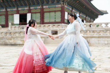 Haziran 2025 'te Seul' de, 20 'li yaşlarda iki Koreli kadın pembe ve gökyüzü mavisi Hanbok giyerek Gyeongbokgung Sarayı' nın geleneksel tuğla kapısının önünde duruyorlardı..