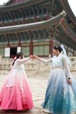Haziran 2025 'te Seul' de, 20 'li yaşlarda iki Koreli kadın pembe ve gökyüzü mavisi Hanbok giyerek Gyeongbokgung Sarayı' nın geleneksel tuğla kapısının önünde duruyorlardı..