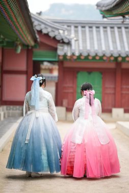 Haziran 2025 'te Seul' de, 20 'li yaşlarda iki Koreli kadın pembe ve gökyüzü mavisi Hanbok giyerek Gyeongbokgung Sarayı' nın geleneksel tuğla kapısının önünde duruyorlardı..