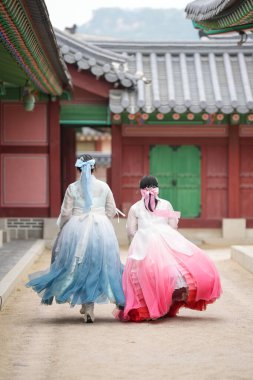 Haziran 2025 'te Seul' de, 20 'li yaşlarda iki Koreli kadın pembe ve gökyüzü mavisi Hanbok giyerek Gyeongbokgung Sarayı' nın geleneksel tuğla kapısının önünde duruyorlardı..
