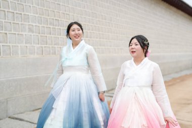 Haziran 'da Seul' de, 30 'lu yaşlarda iki Koreli kadın Gyeongbokgung' daki büyük saray duvarının önünde dikilmiş arkalarında yükselen tarihi taşlar olan parlak pembe ve gökyüzü mavisi Hanbok 'ta sohbet ediyorlardı..
