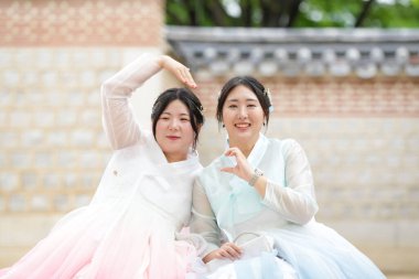 Haziran 'da Seul' de, yirmili yaşlarda iki Koreli kadın Gyeongbokgung Sarayı 'nda çimenli bir plazada otururken, açık bir yaz gökyüzünün altında güzel pembe bir hanbok giyerek elleriyle kalp yapıyorlar. Seul, Haziran.