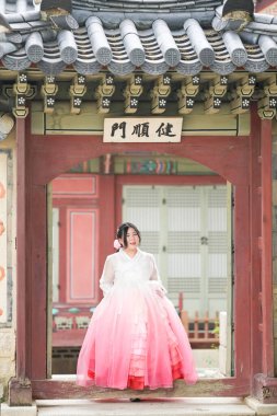 Yirmili yaşlarında Koreli bir kadın Gyeongbokgung Sarayı 'nın süslü kapısının önünde duruyor. Pembe bir şapka takıyor ve parlak bir yaz gökyüzünün altındaki tarihi mimariye hayran. Seul, Haziran.