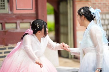 Yirmili yaşlarda iki Koreli kadın Gyeongbokgung Sarayı 'ndaki görkemli tarihi bir yapının yanında el ele tutuşuyor açık bir yaz gökyüzü altında pembe ve gökyüzü mavisi bir Hanbok giyerek gülümsüyorlar. Seul, Haziran.