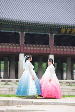 Haziran 'da Seul' de, yirmili yaşlardaki iki Koreli kadın Gyeongbokgung Sarayı 'ndaki tarihi bir salonda poz veriyor, parlak bir yaz gökyüzünün altında pembe ve gökyüzü mavisi bir Hanbok giyiyorlar. Seul, Haziran.