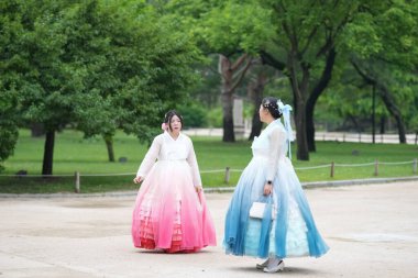 Yirmili yaşlardaki iki Koreli kadın, güzel pembe ve mavi Hanbok 'la yemyeşil bir parkta birlikte yürürken gülüşleri ılık bir yaz gökyüzü altında yankılanırken ışıl ışıl gülümsüyor. Haziran. Seul.