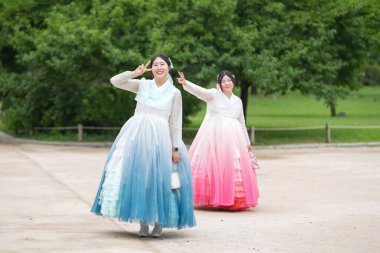 Yirmili yaşlardaki iki Koreli kadın, güzel pembe ve mavi Hanbok 'la yemyeşil bir parkta birlikte yürürken gülüşleri ılık bir yaz gökyüzü altında yankılanırken ışıl ışıl gülümsüyor. Haziran. Seul.