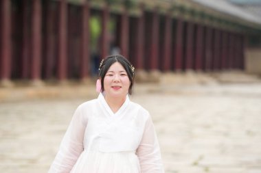 Gyeongbokgung Sarayı 'ndaki parlak bir avluda, yirmili yaşlarda Koreli bir kadın zarif bir şekilde poz veriyor. Açık bir yaz gökyüzü altında büyük, tarihi bir mimariye karşı. Seul, Haziran.