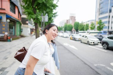 Hareketli bir bulvarda, yirmili yaşlardaki iki Koreli kadın otobüs durağında durup, yumuşak bahar ışığı altında otobüsü beklerken sessizce sohbet ediyorlar. Seul, Jongno Bölgesi, bahar..