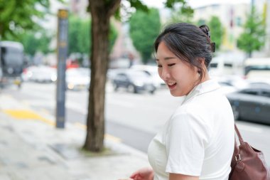 Korna çalan arabaların ve kalabalık kalabalıkların yoğun bulvarında, yirmili yaşlardaki iki Koreli kadın bahar ışığı altındaki bir çantanın içinde hafifçe gülerek arama yapıyorlar. Seul, Jongno Bölgesi, bahar..