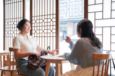 Pencere kenarında ahşap iç mekânları olan şık bir kafede, 20 'li yaşlarındaki iki Koreli kadın sıcak kahvenin üzerinde akıllı telefonları tutarak yumuşak bahar ışığı altında gülüyor. Seul, Jongno Bölgesi, bahar..