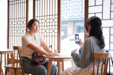 Pencere kenarında ahşap iç mekânları olan şık bir kafede, 20 'li yaşlarındaki iki Koreli kadın sıcak kahvenin üzerinde akıllı telefonları tutarak yumuşak bahar ışığı altında gülüyor. Seul, Jongno Bölgesi, bahar..