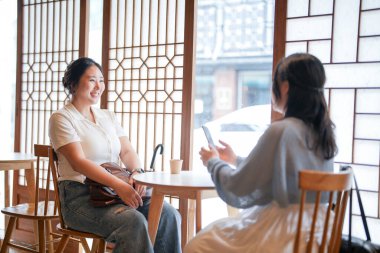 Pencere kenarında ahşap iç mekânları olan şık bir kafede, 20 'li yaşlarındaki iki Koreli kadın sıcak kahvenin üzerinde akıllı telefonları tutarak yumuşak bahar ışığı altında gülüyor. Seul, Jongno Bölgesi, bahar..