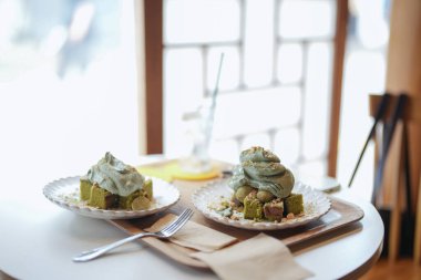 Ahşap kirişleri ve yerden tavana pencereleri olan şık bir kafede, baharın gerçek bir simgesi: güneş ışığında dinlenen mugwort kekleri ve çaylar, hafif esintide sürüklenen yapraklar. Seul Baharı, Jongno Bölgesi.