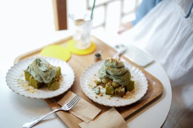 Ahşap kirişleri ve yerden tavana pencereleri olan şık bir kafede, baharın gerçek bir simgesi: güneş ışığında dinlenen mugwort kekleri ve çaylar, hafif esintide sürüklenen yapraklar. Seul Baharı, Jongno Bölgesi.