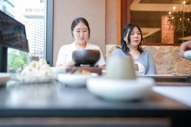 Güneşli bir pencere masasındaki bir kalp barbekü restoranında, 20 'li yaşlardaki iki Koreli kadın hafif bahar ışığı altında ızgara et ve meze yemekten hoşlanıyorlar. Seul, Jung Bölgesi, bahar..