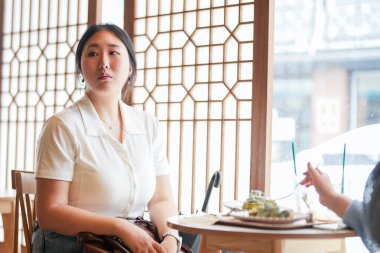 Pencere kenarındaki şık bir kafede, yirmili yaşlardaki sıradan elbiseli iki Koreli kadın içki ve şekerlerle oturur, yumuşak bahar ışığı altında gülüp sohbet ederler. Seul, Jongno Bölgesi, bahar..