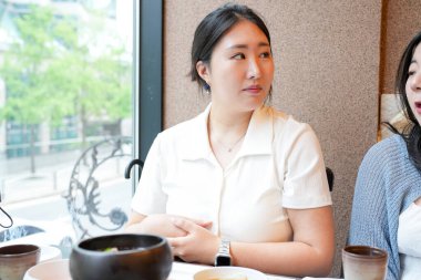 Güneşli bir pencere masasındaki bir kalp barbekü restoranında, 20 'li yaşlardaki iki Koreli kadın hafif bahar ışığı altında ızgara et ve meze yemekten hoşlanıyorlar. Seul, Jung Bölgesi, bahar..